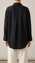 Black oversized shirt with back yoke, box pleat and curved shirt-tail hem, worn by a model, back view
