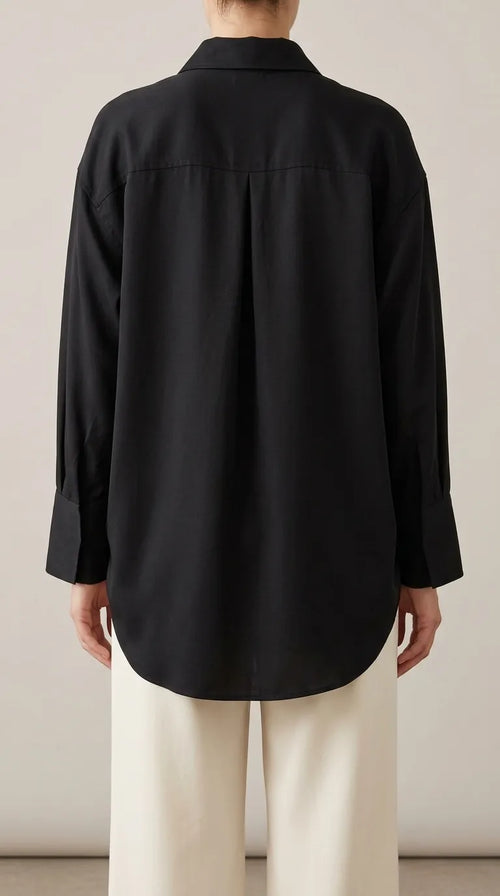 Black oversized shirt with back yoke, box pleat and curved shirt-tail hem, worn by a model, back view