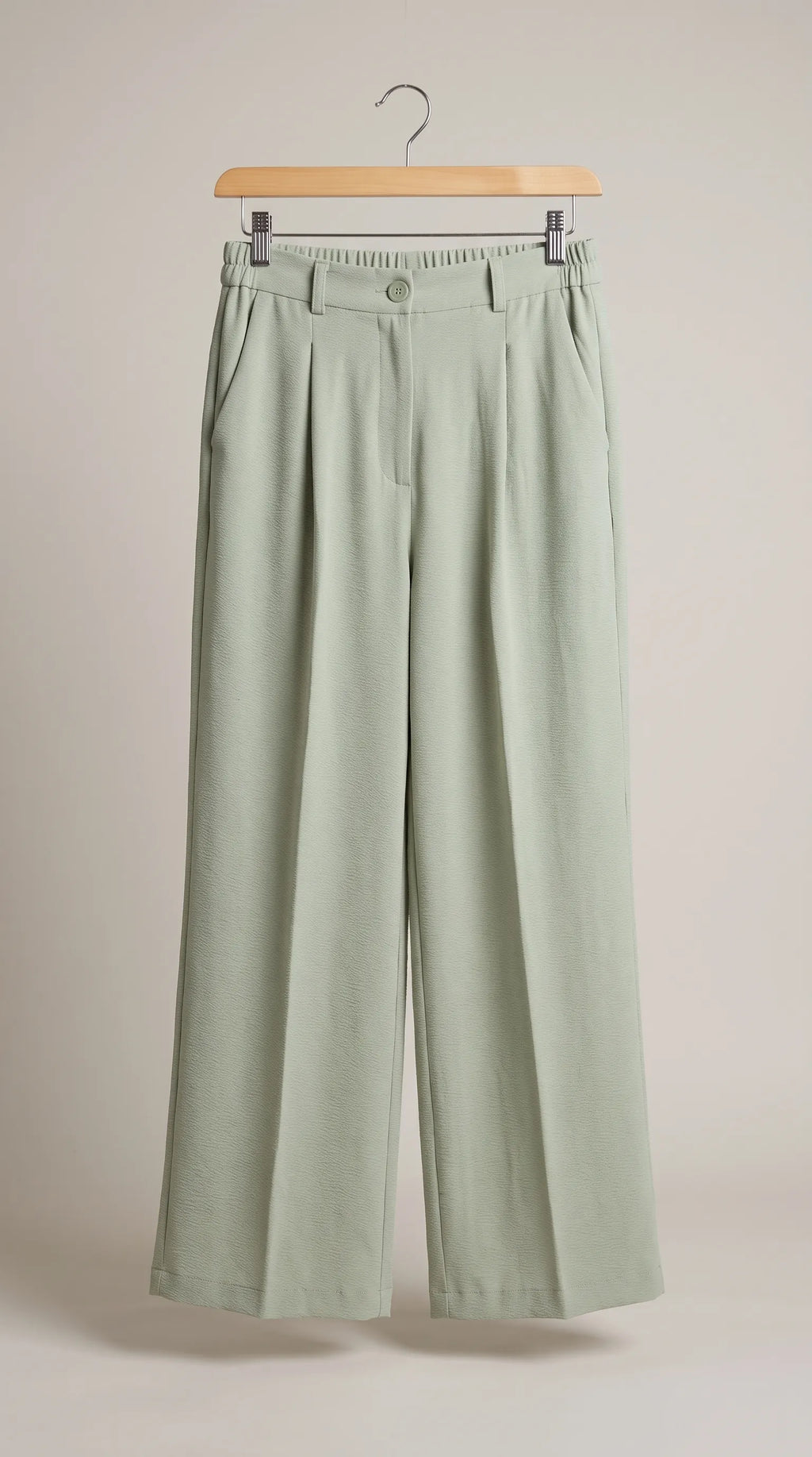 Matcha sage-green pleated wide-leg trousers hanging on a hanger, front view