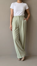 Matcha sage-green wide-leg trousers worn by a model leaning against a wall, front view