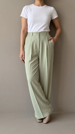 Matcha sage-green wide-leg trousers worn by a model leaning against a wall, front view