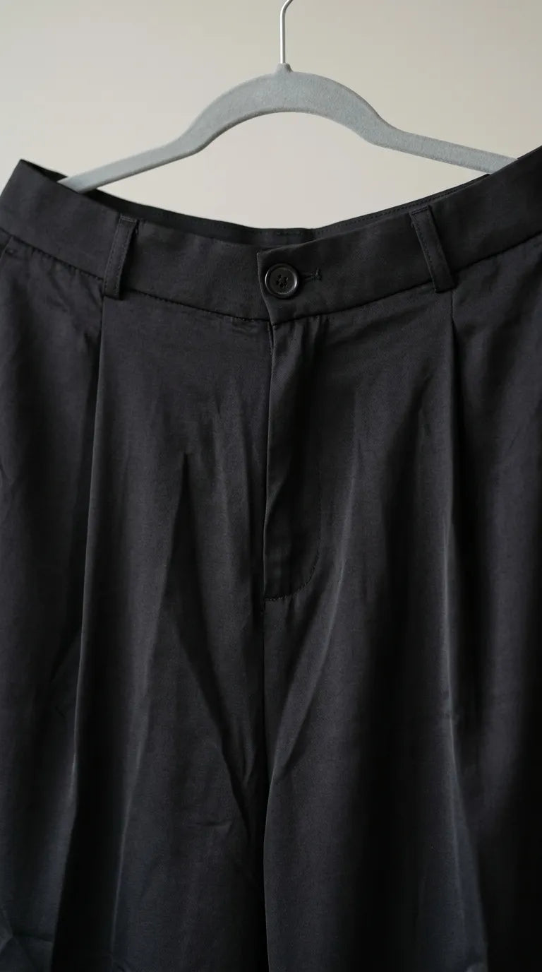 Close-up of the black trousers' waistband, button and front pleat
