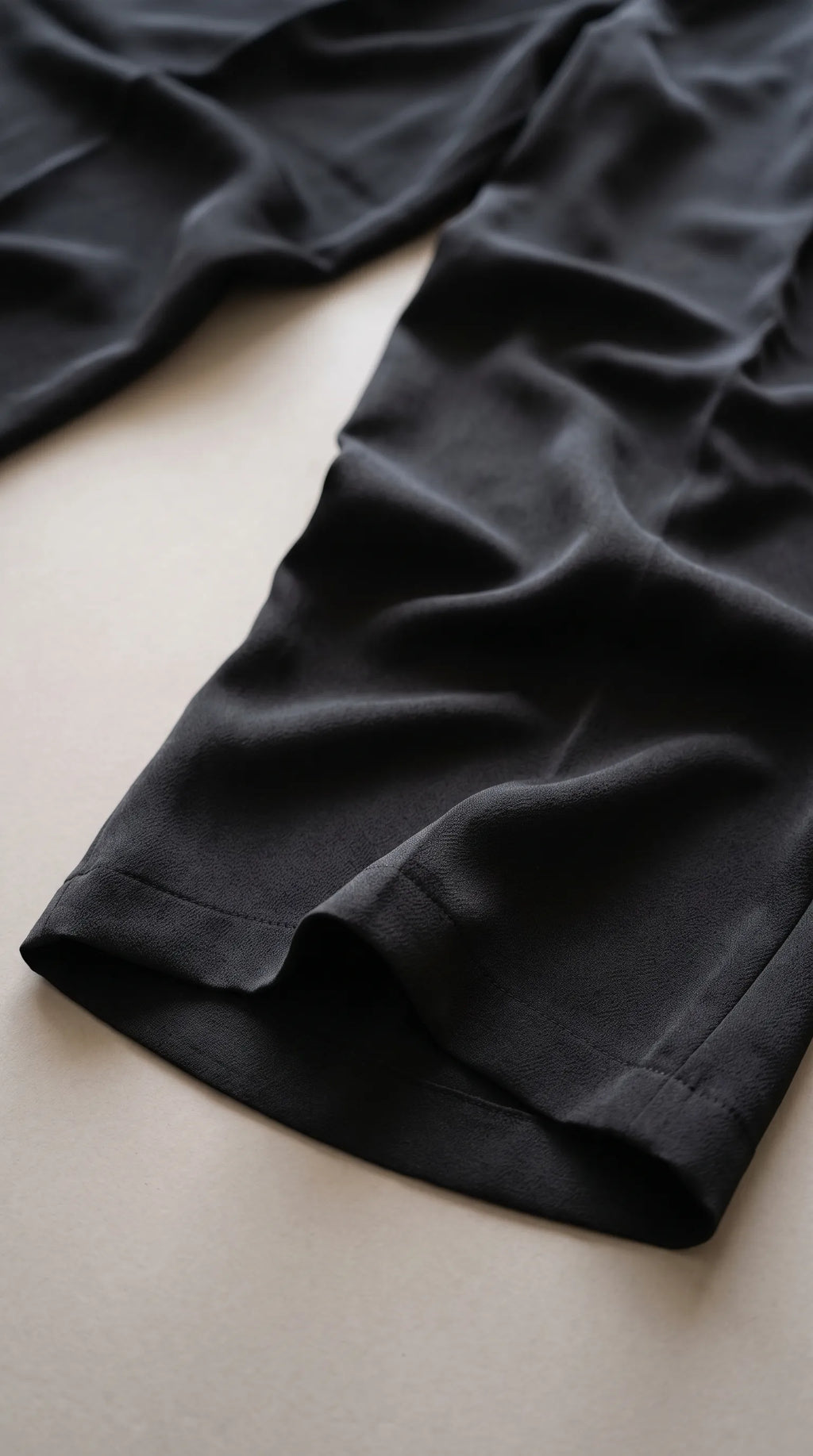 Close-up of the black satin-crepe trousers' fabric and hem