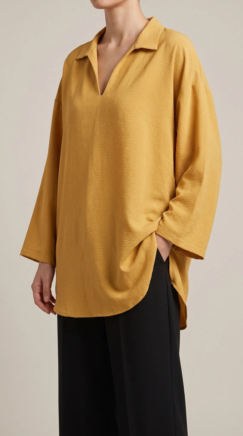 Mustard oversized V-neck tunic worn by a model with one hand in her trouser pocket, three-quarter view