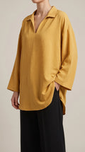 Mustard oversized V-neck tunic worn by a model with one hand in her trouser pocket, three-quarter view