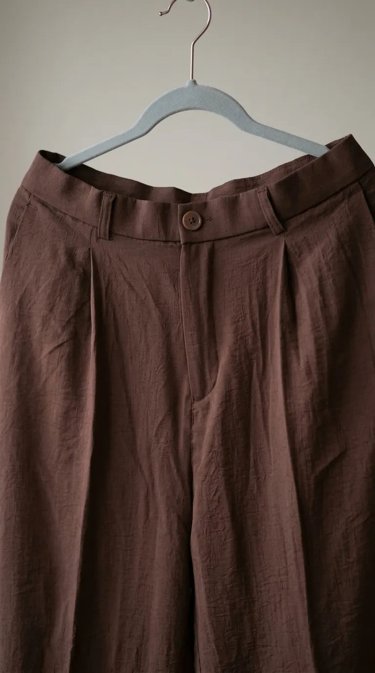 Close-up of the brown trousers' waistband, button and pleats