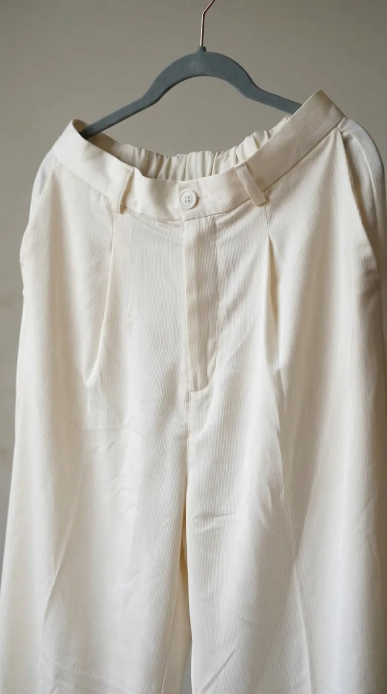 Close-up of the ivory trousers' waistband, button and pleat